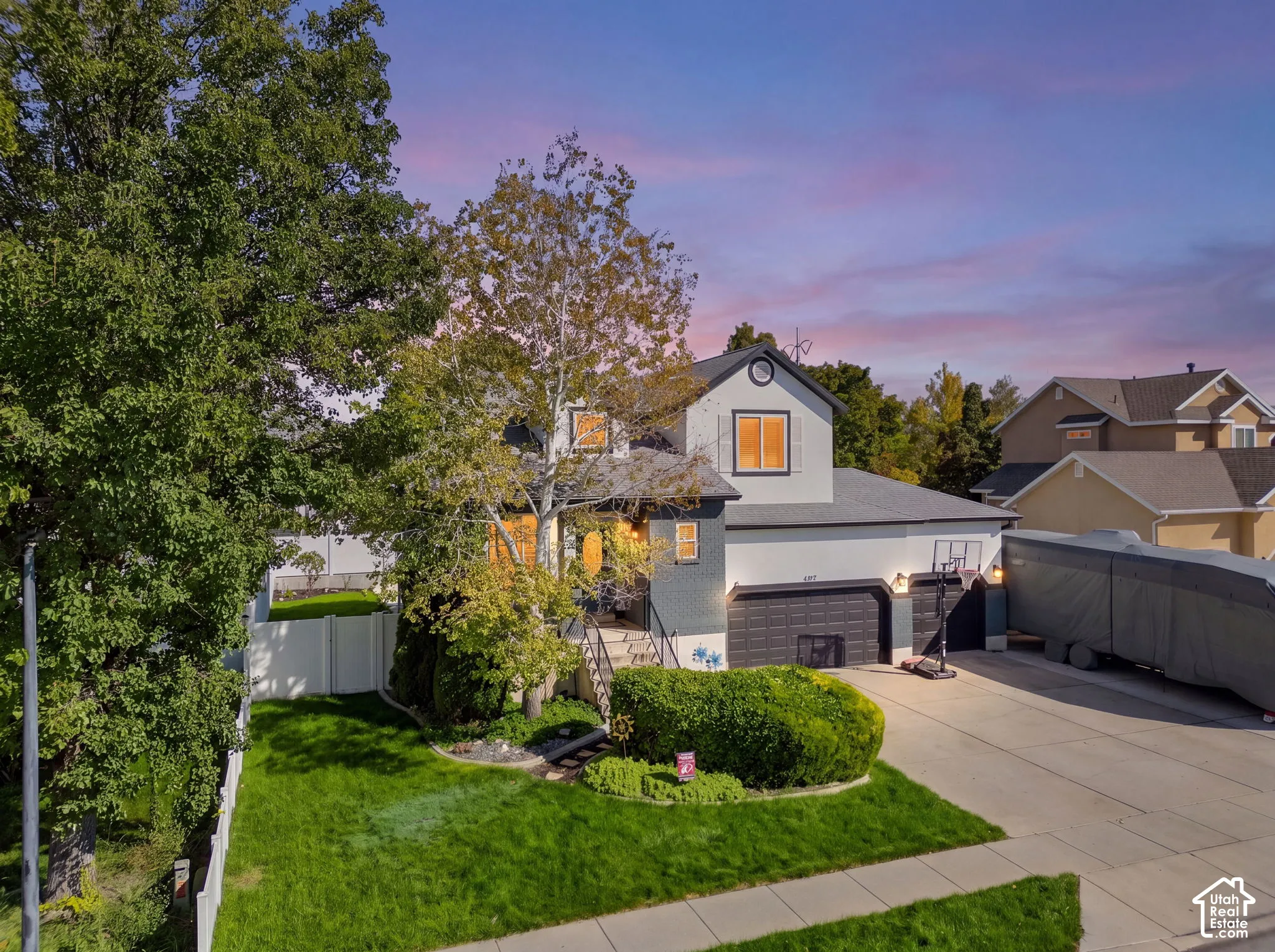 Manicured lawn with mature trees, a paved driveway, and a two-car garage