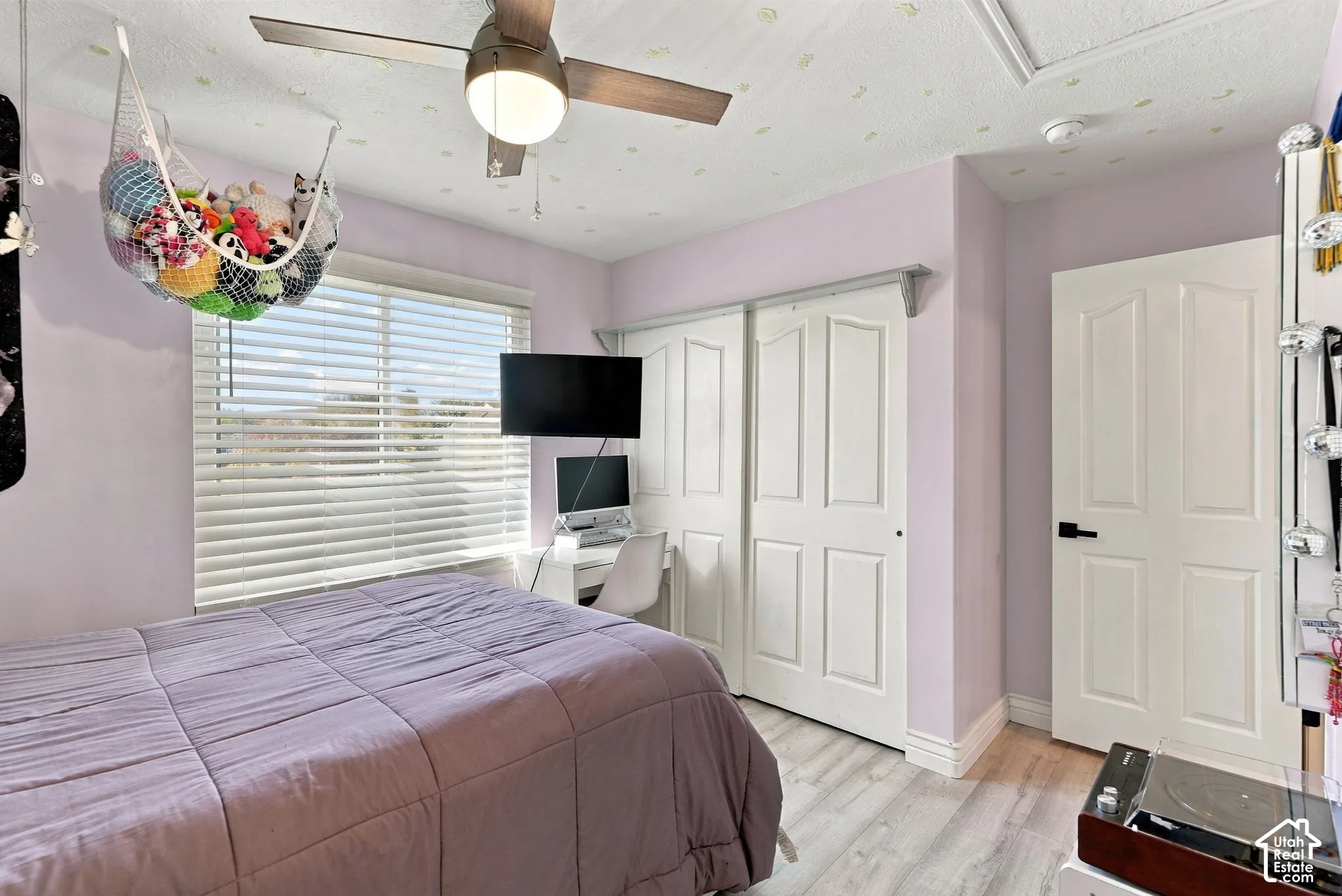 Wood-finish flooring, ceiling fan with integrated lighting, sliding closet doors, and window with horizontal blinds
