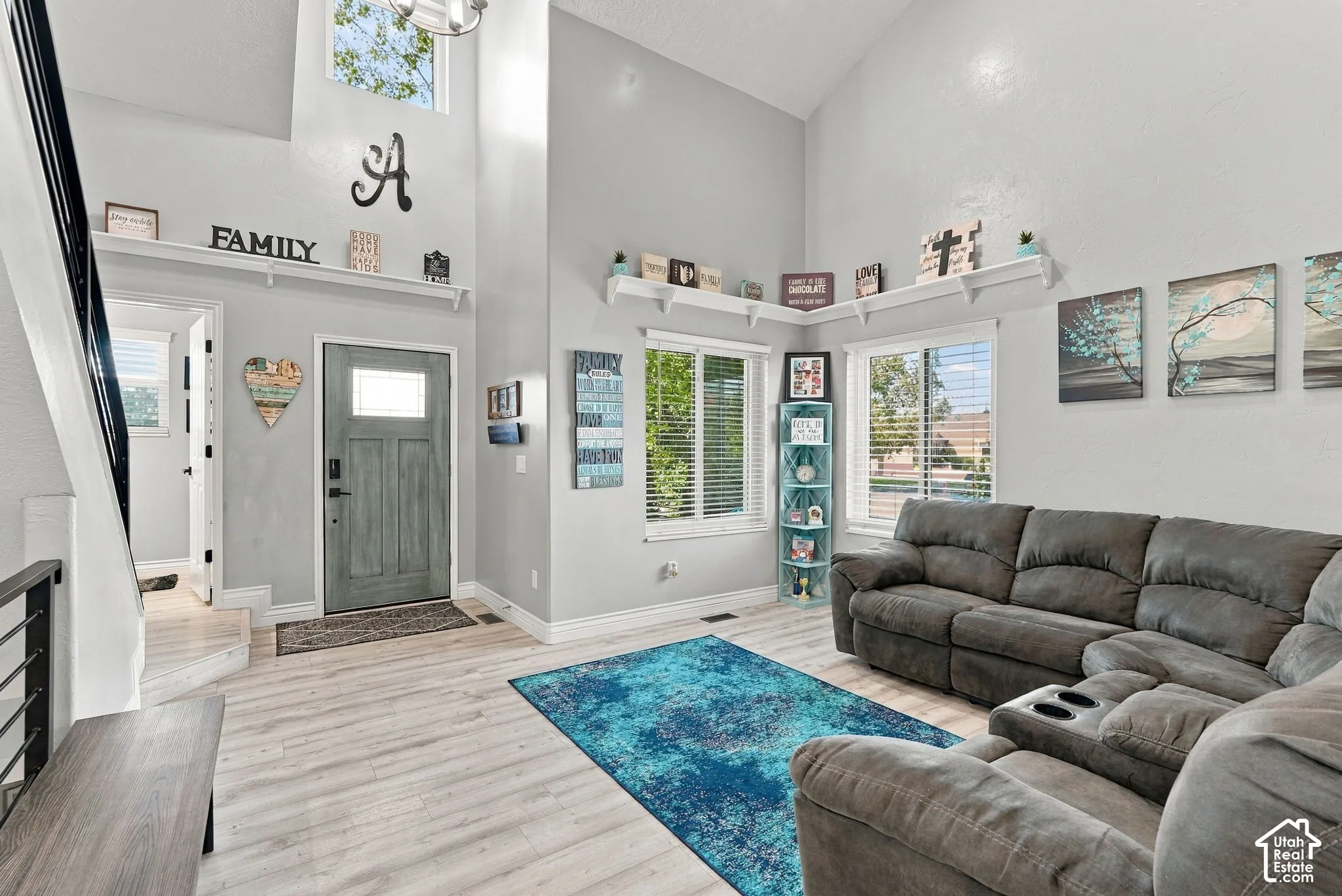 Vaulted ceiling, wood-finish flooring, staircase with dark handrail, abundant natural light, and a paneled entry door