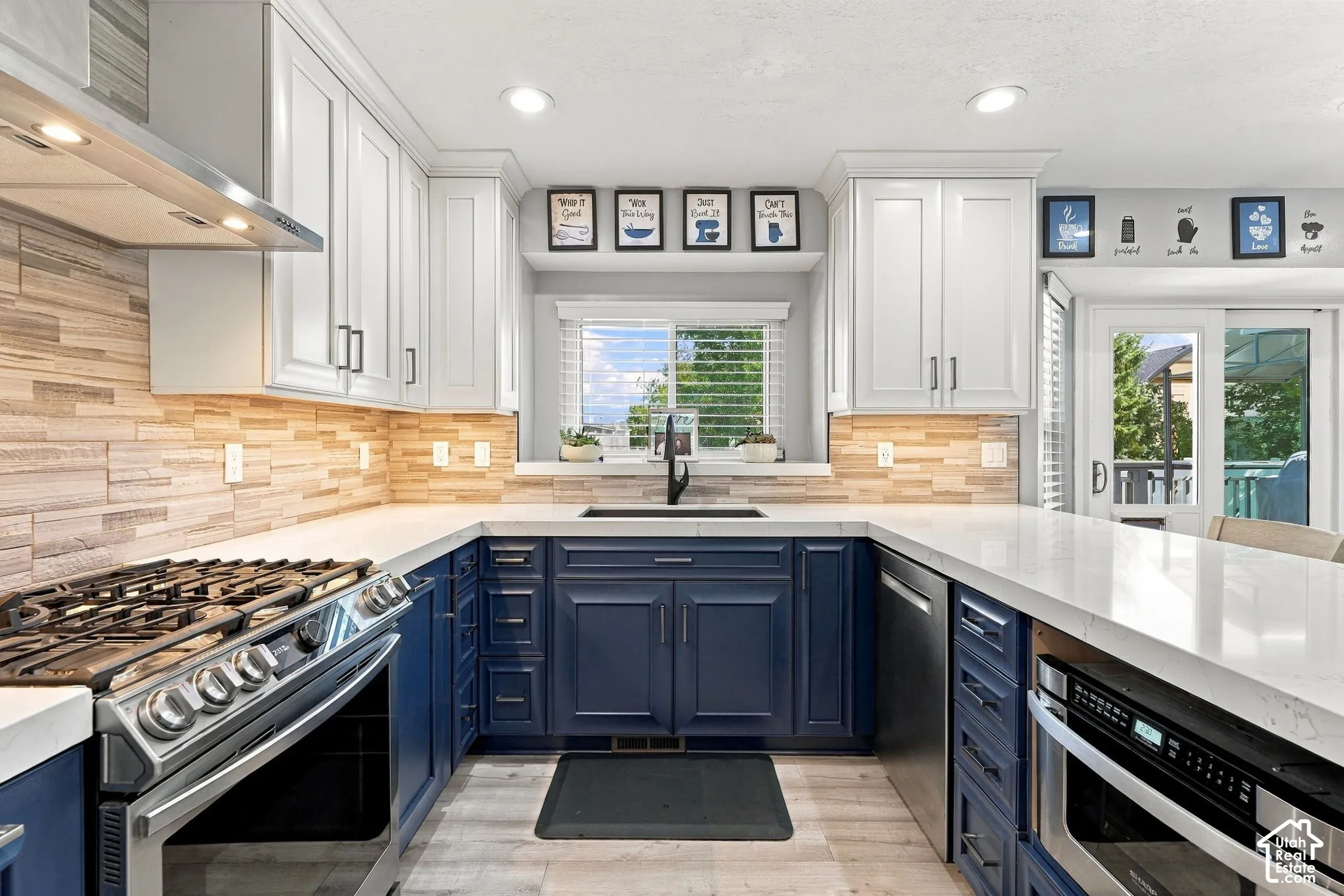 Two-tone cabinetry, stainless steel range, built-in microwave, wood-finish backsplash, and light countertops