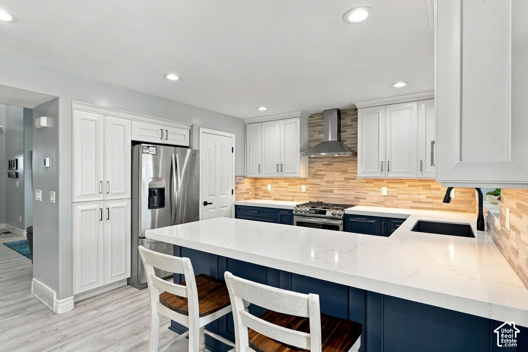 Kitchen featuring white upper cabinetry, blue lower cabinetry, stainless steel appliances, a white island countertop, and light wood-finish flooring