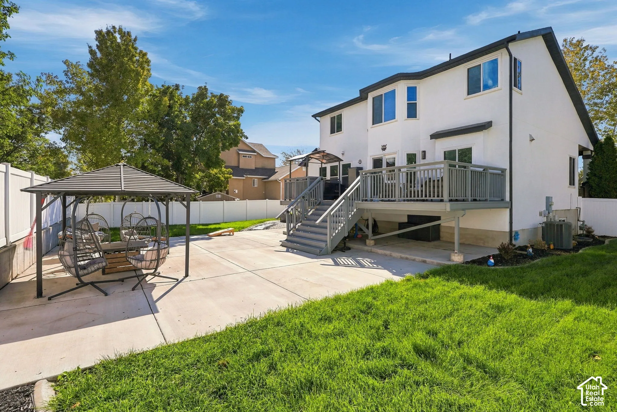 White exterior with multiple windows, elevated deck with railings, and ground-level concrete patio