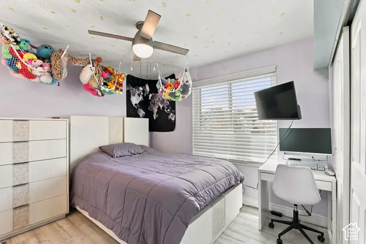 Wood-finish flooring, ceiling fan, window with horizontal blinds, built-in closet with sliding doors, and a built-in desk