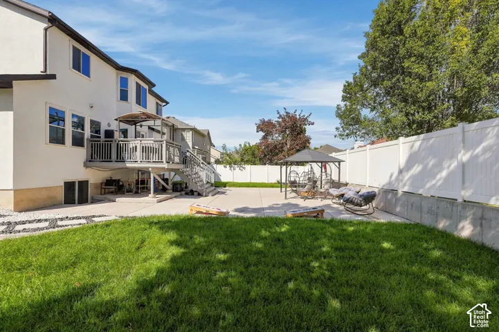 Expansive backyard featuring a manicured lawn, a large concrete patio, a multi-level deck, and a white privacy fence