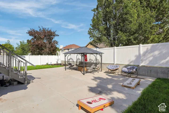 Expansive concrete patio with a permanent gazebo structure, bordered by a white privacy fence and sections of manicured lawn