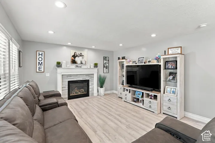 Recessed lighting, wood-finish flooring, fireplace with stone surround, and window with blinds