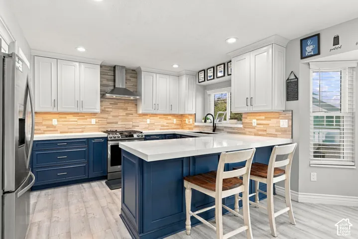 Two-tone cabinetry with white upper and blue lower cabinets, white countertops, wood-finish flooring, stainless steel appliances, and a central island with seating