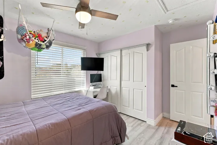 Wood-finish flooring, ceiling fan with integrated lighting, sliding closet doors, and window with horizontal blinds