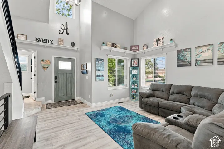 Vaulted ceiling, wood-finish flooring, staircase with dark handrail, abundant natural light, and a paneled entry door