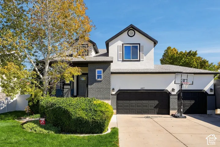 Exterior featuring a two-car garage, gray brick accents, white stucco siding, and a paved driveway
