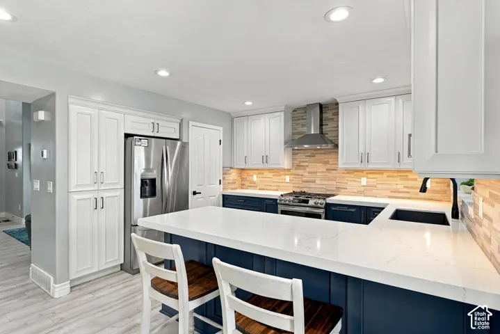 Kitchen featuring white upper cabinetry, blue lower cabinetry, stainless steel appliances, a white island countertop, and light wood-finish flooring