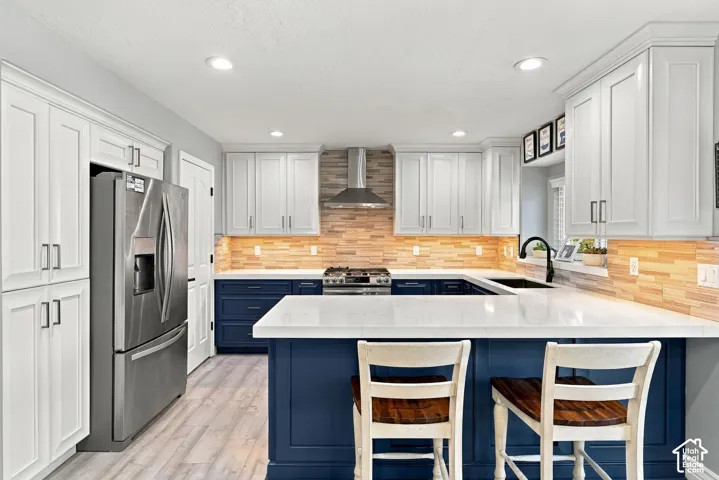 Kitchen featuring white upper cabinetry, navy base cabinetry, light wood-finish backsplash, stainless steel appliances, and a central island with white countertops