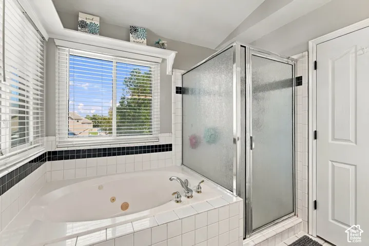 White tiled jetted tub with chrome fixtures, frosted glass shower enclosure, and windows with horizontal blinds
