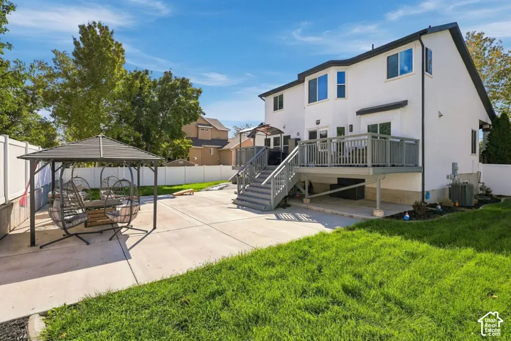 White exterior with multiple windows, elevated deck with railings, and ground-level concrete patio
