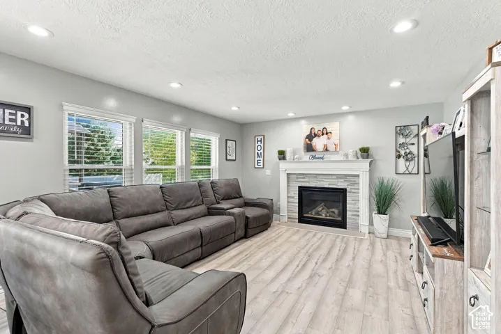 Recessed lighting, wood-finish flooring, multiple windows with blinds, built-in fireplace with stone surround and mantle, and light-toned wall paint