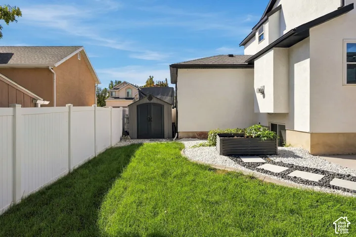 Expansive grassy area, white vinyl fencing, storage shed, raised garden bed, and a stone pathway