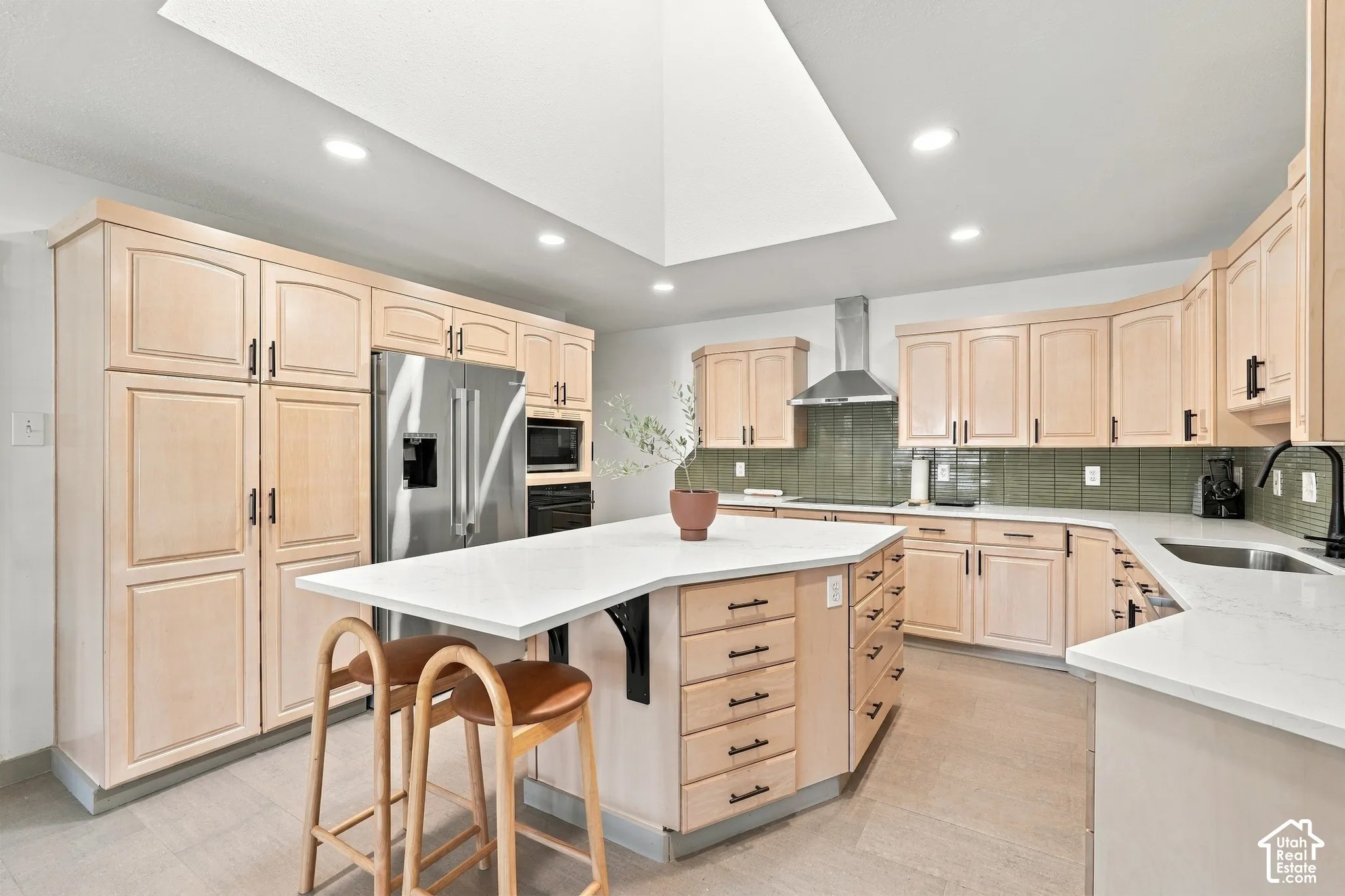 Spacious kitchen featuring light wood cabinetry, a central island with a white countertop, a stainless steel refrigerator, and a green tile backsplash