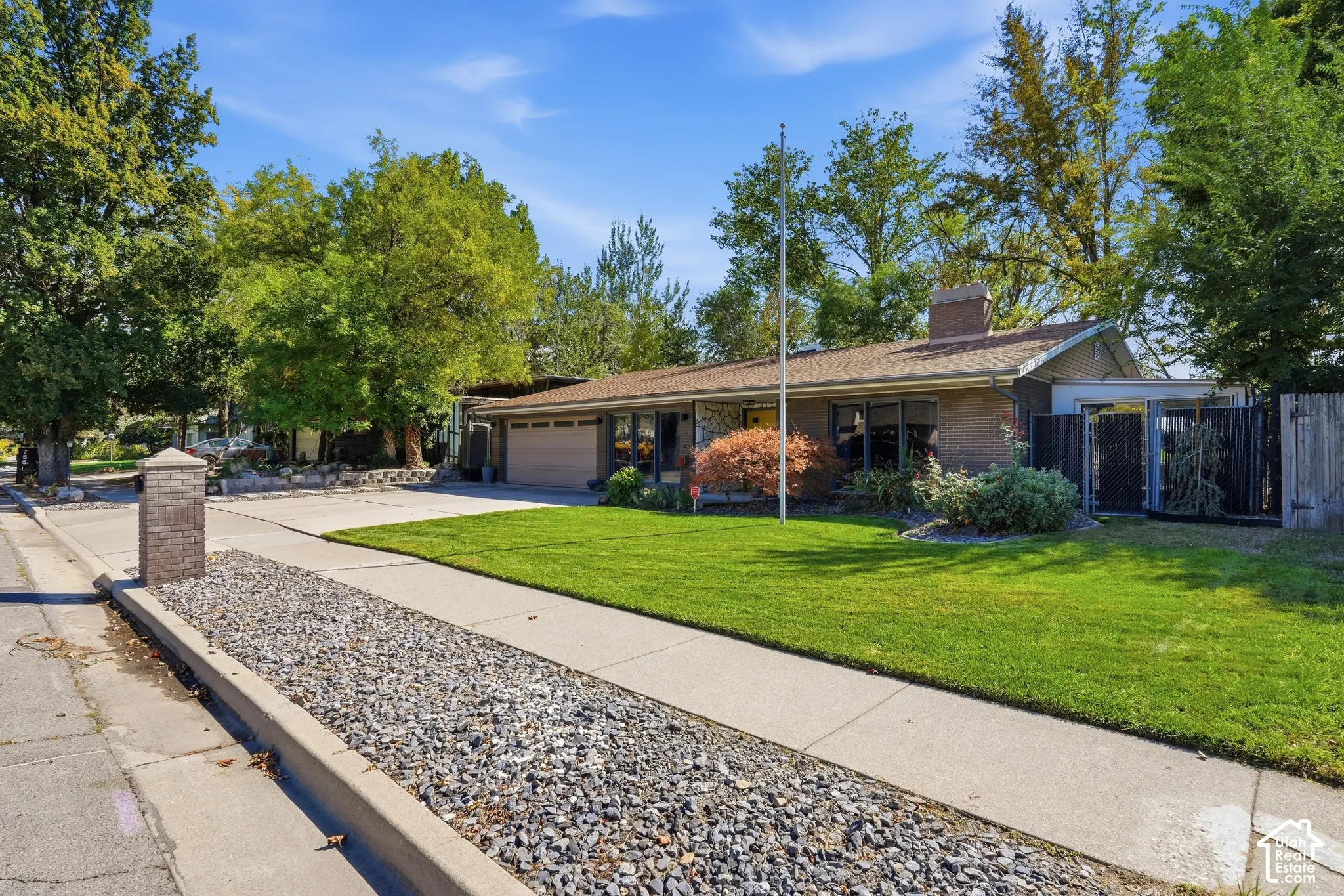 Brick exterior with a prominent chimney, attached two-car garage, mature landscaping, and an expansive lawn
