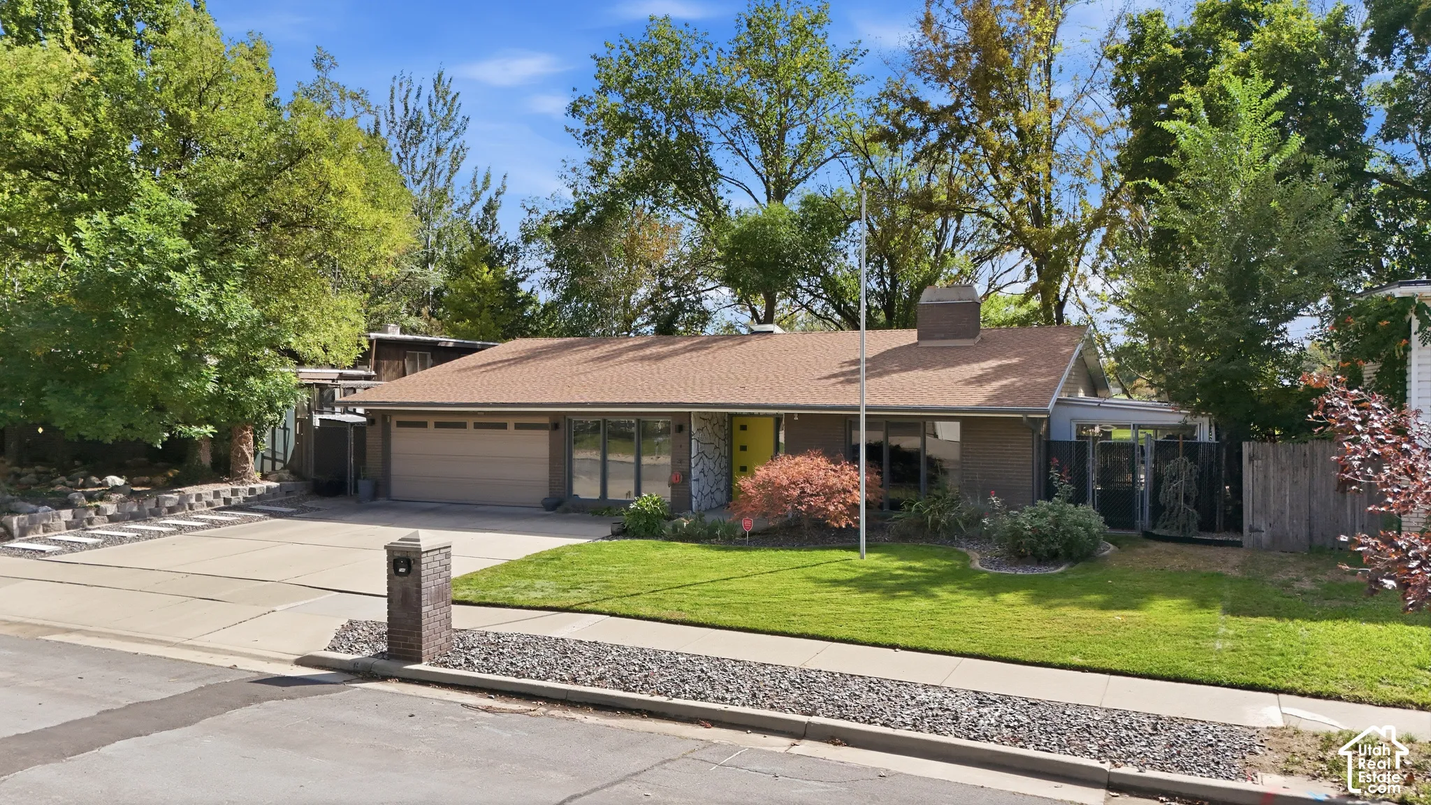 Ranch-style residence featuring a prominent garage, a low-pitched roof, and mature landscaping
