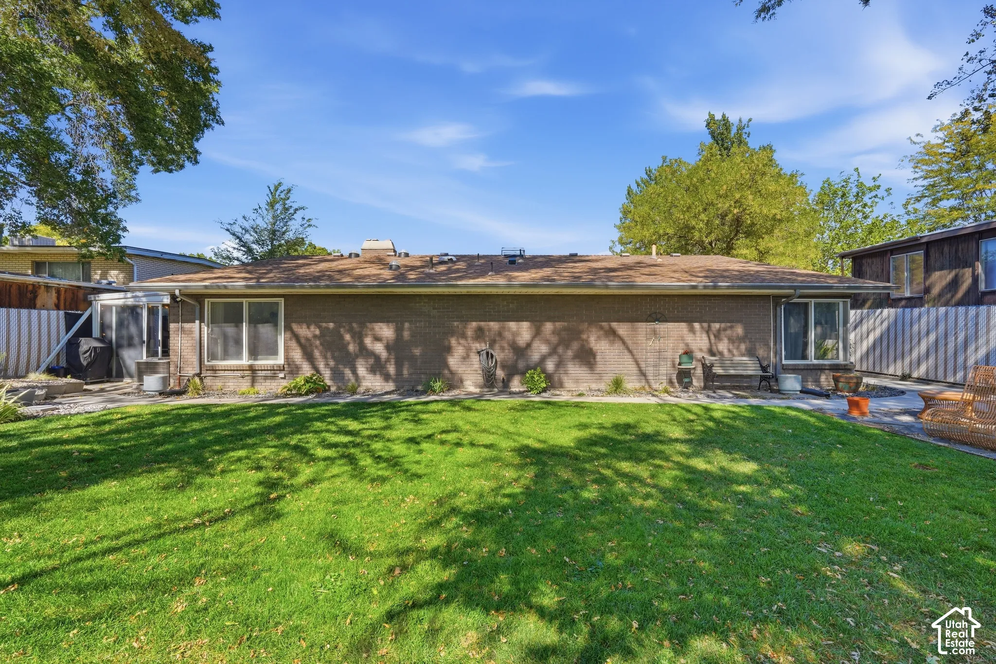 Expansive backyard featuring a manicured lawn, brick exterior, multiple windows, and a paved patio area