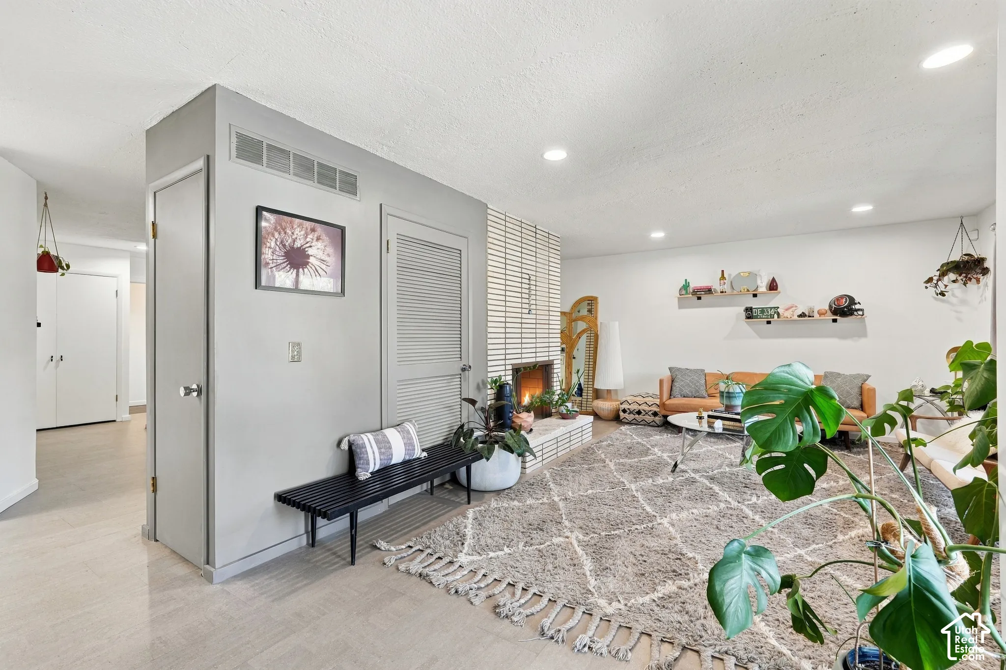 Recessed lighting throughout, white brick fireplace, light-toned flooring, and floating shelves