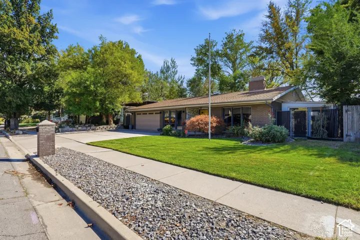 Brick exterior with a prominent chimney, attached two-car garage, mature landscaping, and an expansive lawn