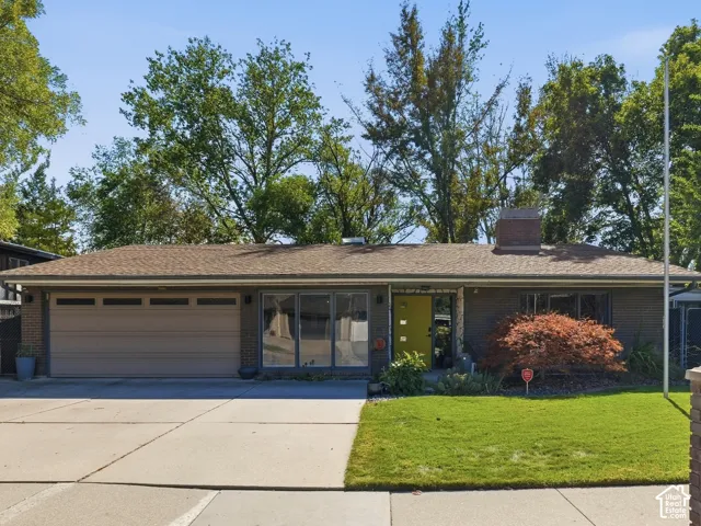 Single-story residence featuring an attached two-car garage, expansive concrete driveway, brick exterior accents, and a manicured lawn