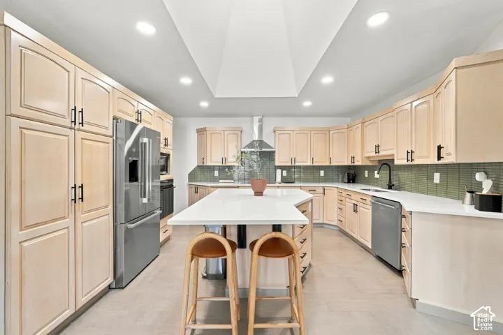 Kitchen featuring light wood cabinetry, stainless steel appliances, a center island with countertop, a green tiled backsplash, and recessed lighting