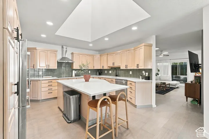 Spacious kitchen featuring an island with seating, stainless steel appliances, light wood-finish cabinetry, a large skylight, and recessed lighting