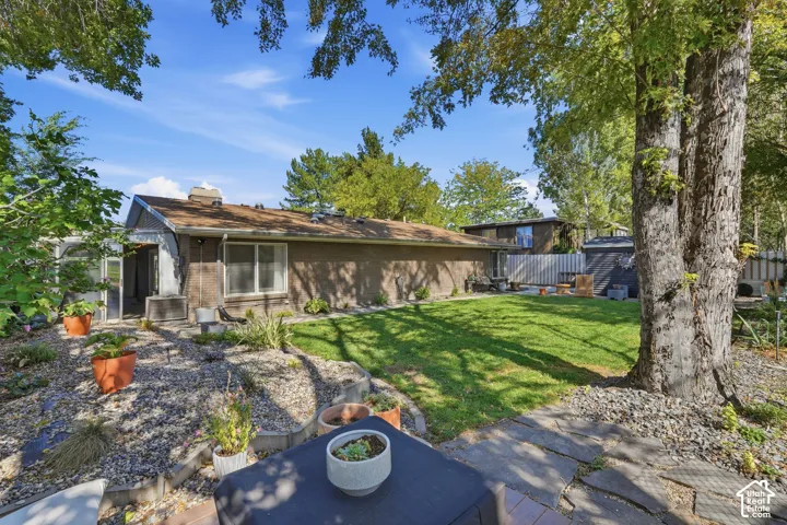 Expansive outdoor space featuring a stone patio, gravel landscaping, a manicured lawn, mature trees, and a screen-enclosed porch