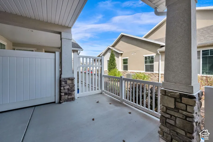 Covered patio area featuring a privacy fence, white picket railing, and stone-clad columns