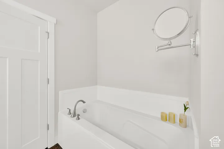 Built-in bathtub with deck-mounted brushed nickel faucet, clean white tiling, and a panel door
