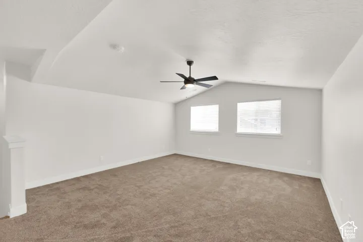 Vaulted ceiling with a contemporary ceiling fan, two windows with blinds, and neutral carpet flooring