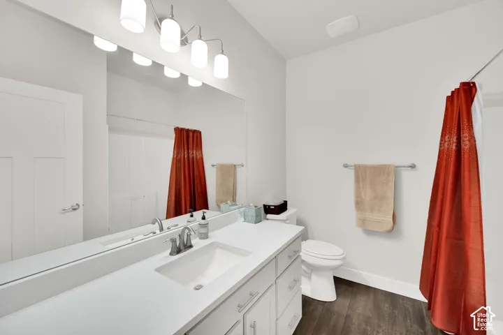 Bathroom featuring a single vanity with an undermount sink, a large mirror, a chrome faucet, a shower with a curtain rod, and wood-finish flooring