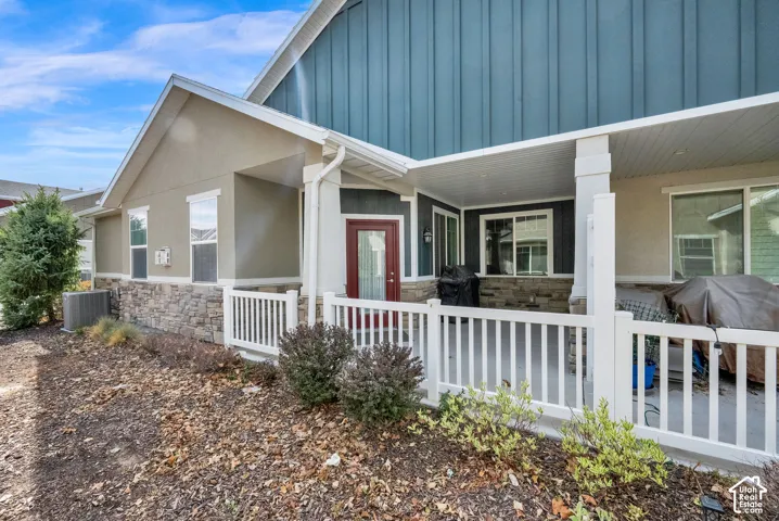 Covered front porch featuring white railings, stone and stucco exterior, and a red entry door