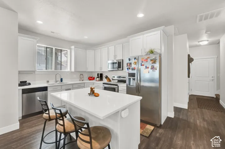 Kitchen featuring white cabinetry, stainless steel appliances, a white island with countertop seating, and wood-finish flooring