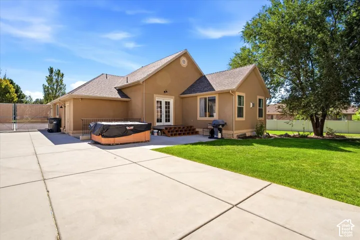 Stucco exterior with a pitched roof, double french doors, concrete patio, and a manicured lawn