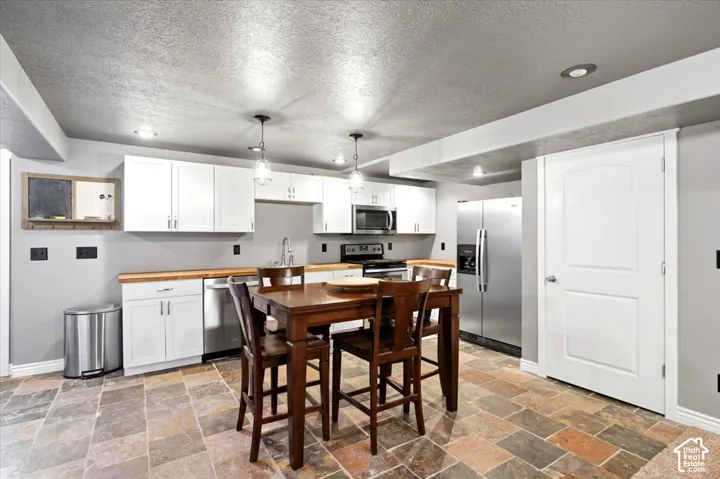 White cabinetry, wood-finish countertops, stainless steel appliances, recessed lighting, and stone tile flooring
