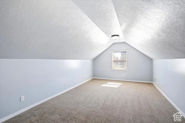 Carpeted room with a pitched ceiling, a single window, and a flush mount light fixture