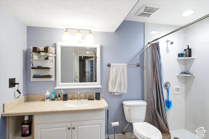 Bathroom featuring a single vanity with a laminate countertop, white cabinetry, a wall-mounted medicine cabinet, and a tiled shower with a shower curtain rod
