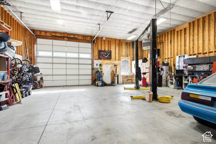 Expansive garage featuring a large paneled overhead door, concrete flooring, exposed wood-stud walls, and a visible vehicle lift system