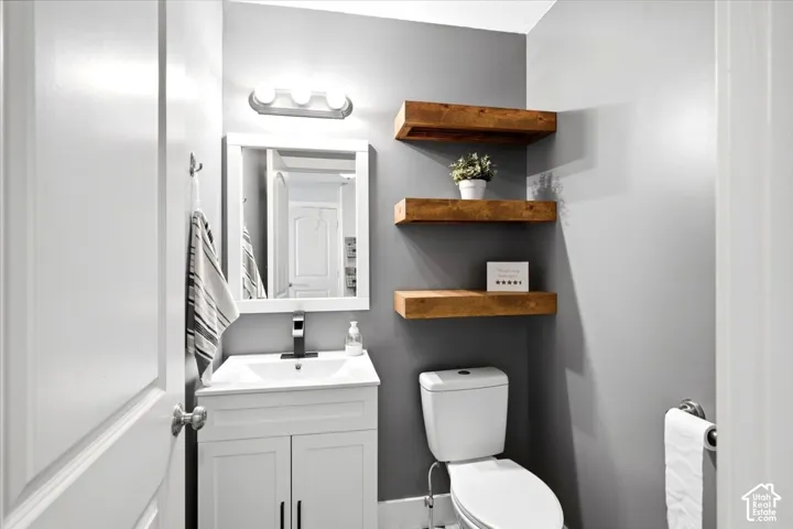 White vanity with integrated sink, rectangular framed mirror, three-light vanity bar, and three wood-finish floating shelves
