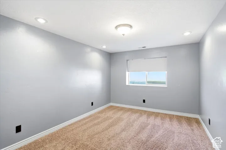 Recessed lighting, central ceiling light fixture, window with roller shade, light gray painted walls, and textured carpet flooring