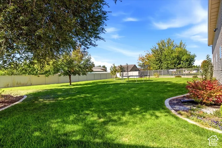 Expansive backyard featuring a manicured lawn, established trees, mature landscaping, and a privacy fence