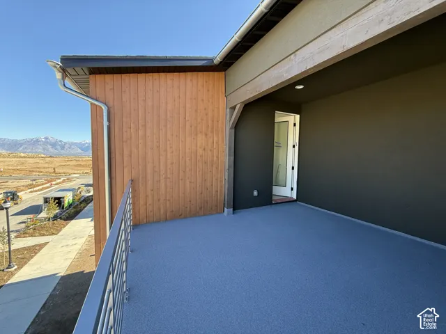 Spacious outdoor balcony with a light blue textured surface, featuring a modern metal railing, wood-paneled exterior siding, and a mountain backdrop