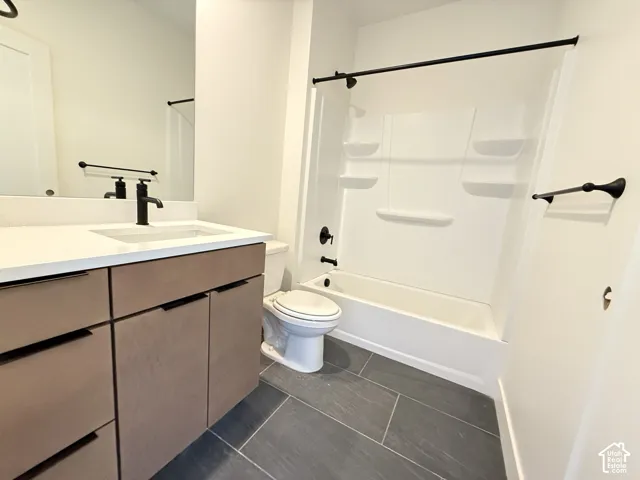 White subway tile shower surround with black fixtures, dark tile flooring, and a vanity with a white countertop