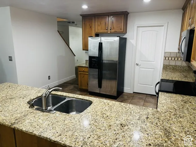 Granite countertops, stainless steel appliances, wood-finish cabinetry, tile flooring, and a dual basin sink with a gooseneck faucet