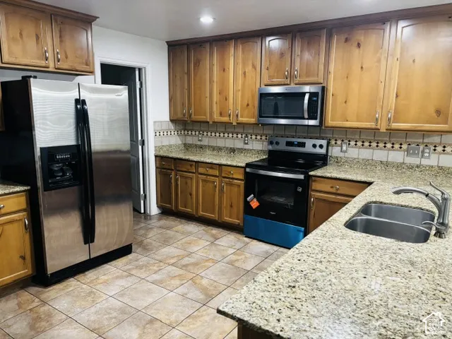Kitchen featuring wood cabinetry, stainless steel appliances, granite-style countertops, and a decorative tile backsplash