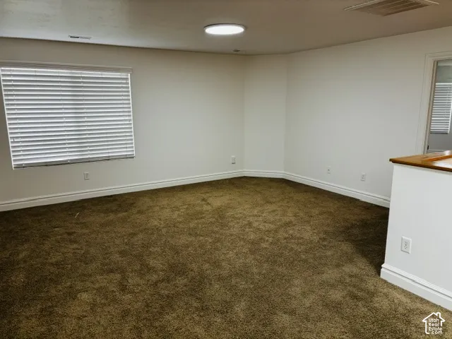 Carpeted interior space with white walls, a large window with horizontal blinds, and a built-in wood-top half wall
