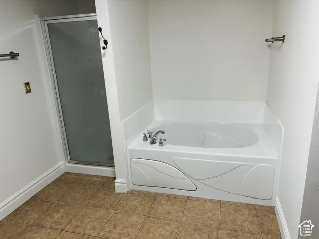 Built-in soaking tub with chrome fixtures, enclosed shower, and tile flooring